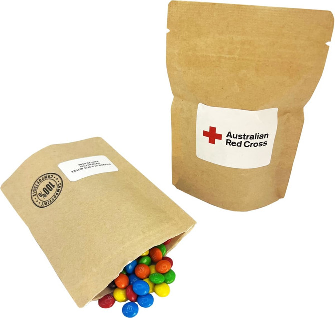 A compostable bag containing colourful M&Ms spilling out, with a simple natural kraft design and a logo.