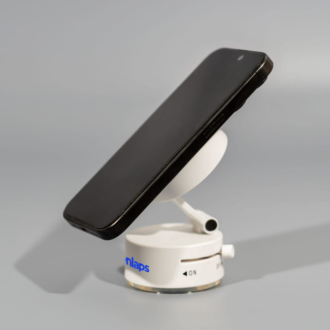 A white vacuum suction magnetic phone stand holding a black smartphone, featuring a circular base and adjustable arm.