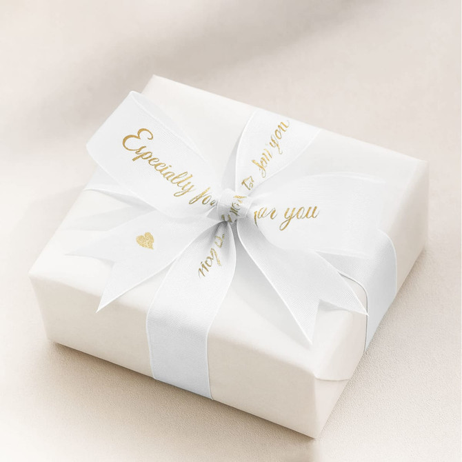A white wrapped gift box adorned with a gold-printed organza ribbon and a decorative bow.