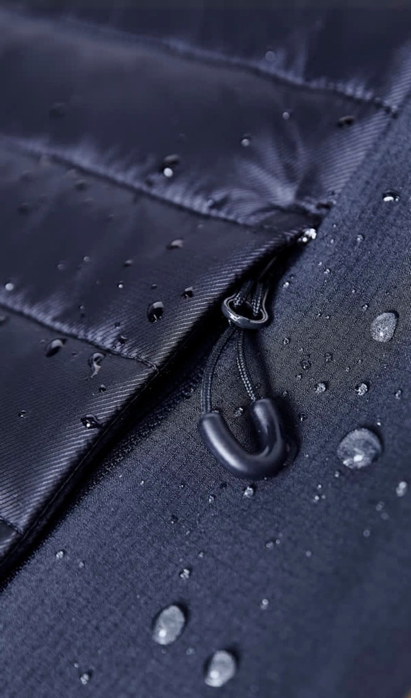 A close-up of a black soft shell jacket featuring a zip and water droplets on its surface.