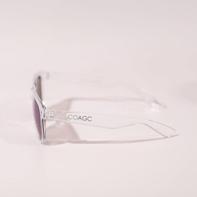 A pair of clear-frame sunglasses with purple lenses, featuring a logo on the side.