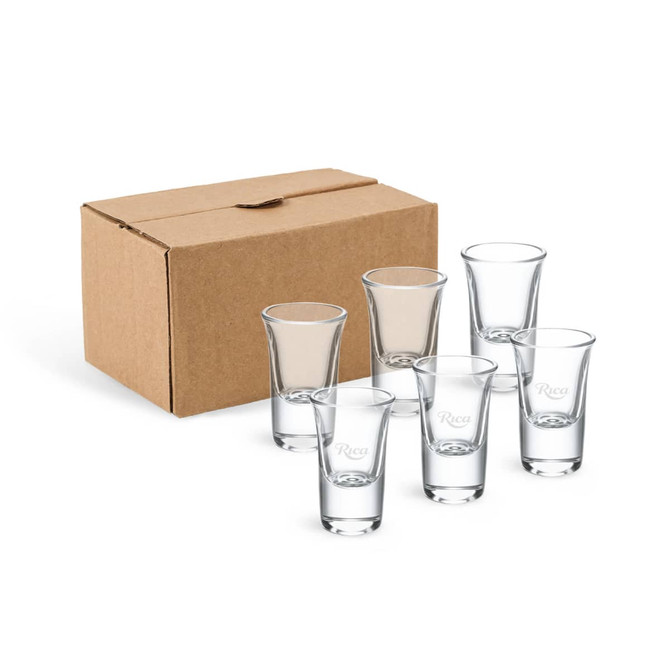 A set of six clear glass shot glasses displayed in front of a brown cardboard box.