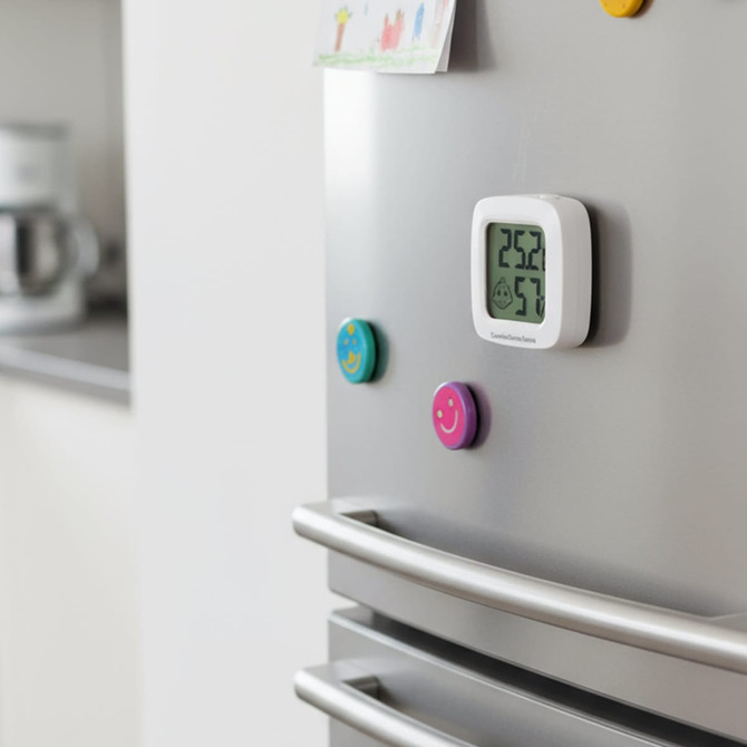 A white mini digital thermometer and hygrometer attached to a silver fridge, displaying temperature and humidity readings.
