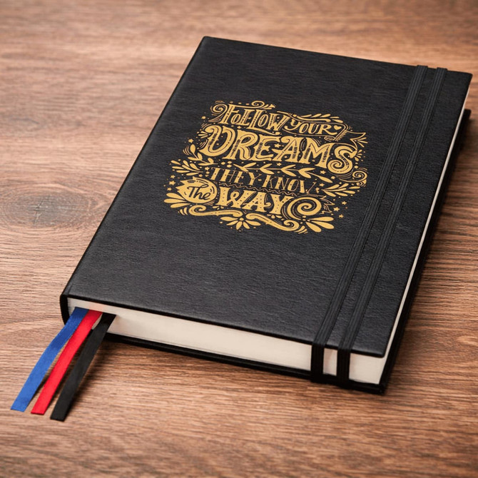 A black diary featuring a decorative gold design and multiple ribbon bookmarks in red, white, and blue.