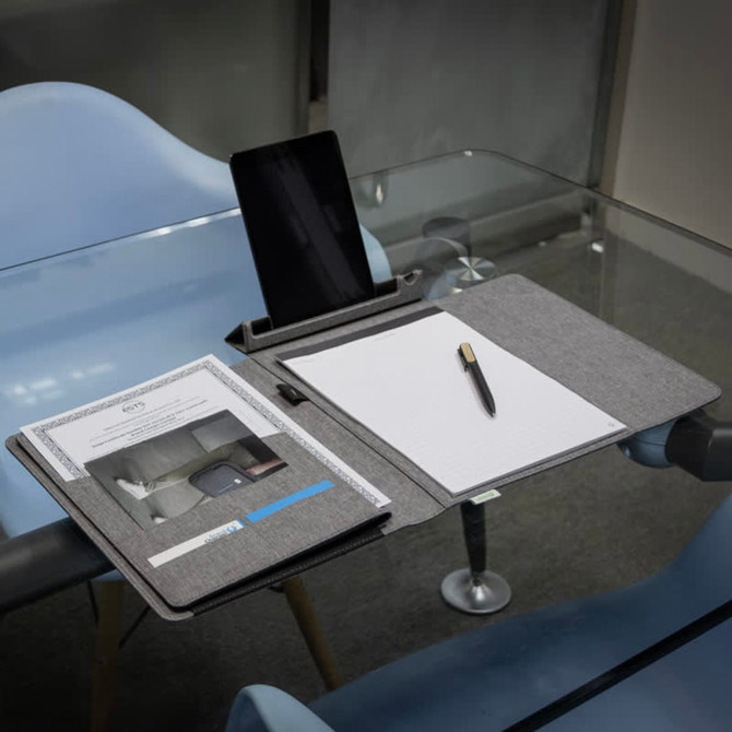 A grey business folio displayed on a table, featuring a tablet stand, notepad, and pen.