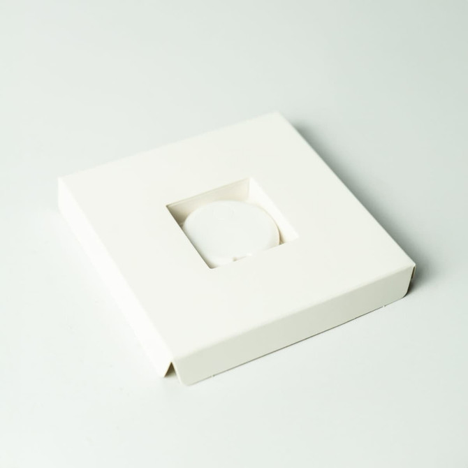 A white square packaging box containing a circular item tracker with a logo.