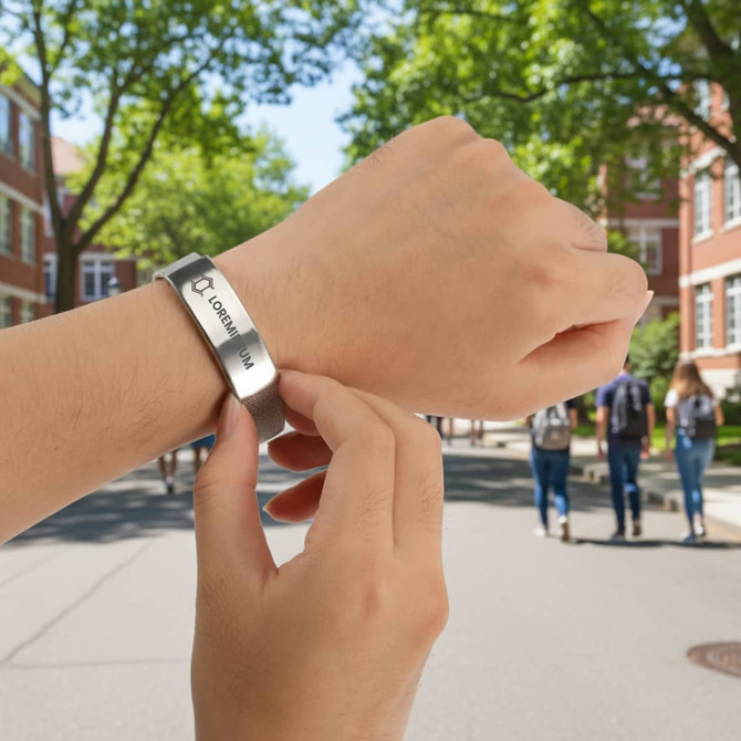 A metal bracelet being adjusted on a wrist, set against a background of trees and a campus pathway.