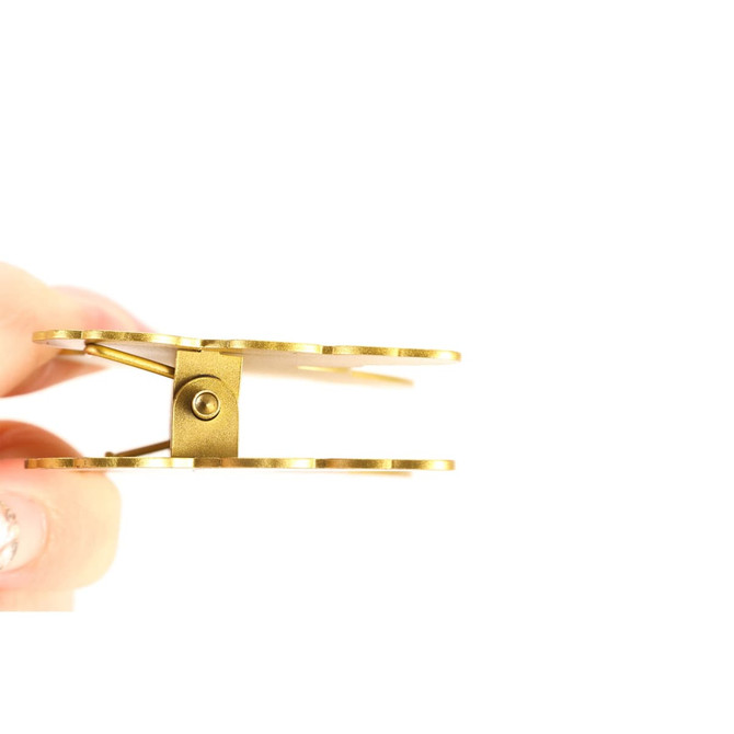 A custom metal clip with a shiny gold finish, held between fingers, showcasing its design and hinge mechanism.