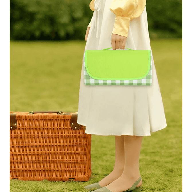 A green and checkered picnic blanket is held by a person wearing a white skirt, standing beside a wicker basket.