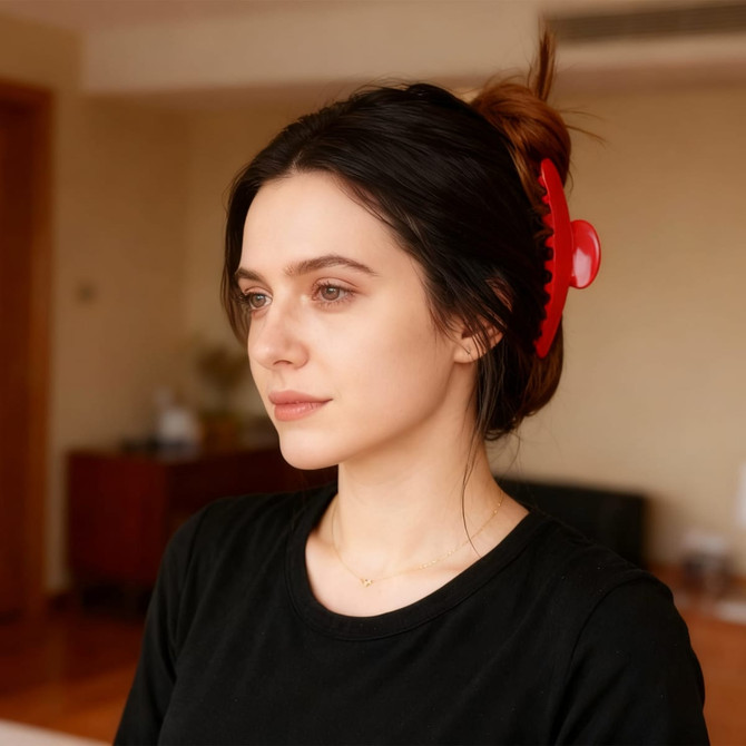 A hair clip in vibrant red is seen in a woman's dark hair, styled in a bun, set in a softly lit interior space.