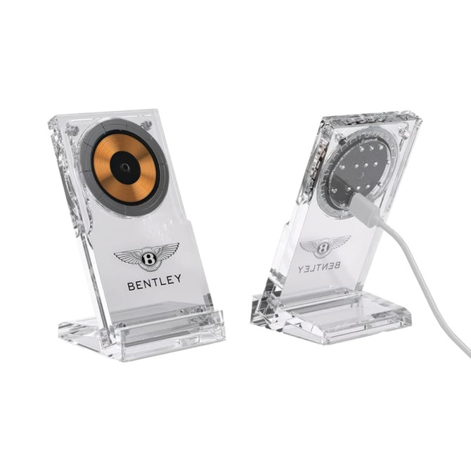A clear acrylic magnetic wireless charging stand with a gold and black circular charging pad. It features a logo.