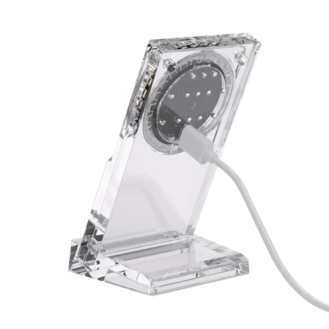A transparent acrylic magnetic wireless charging stand with a white charging cable connected.