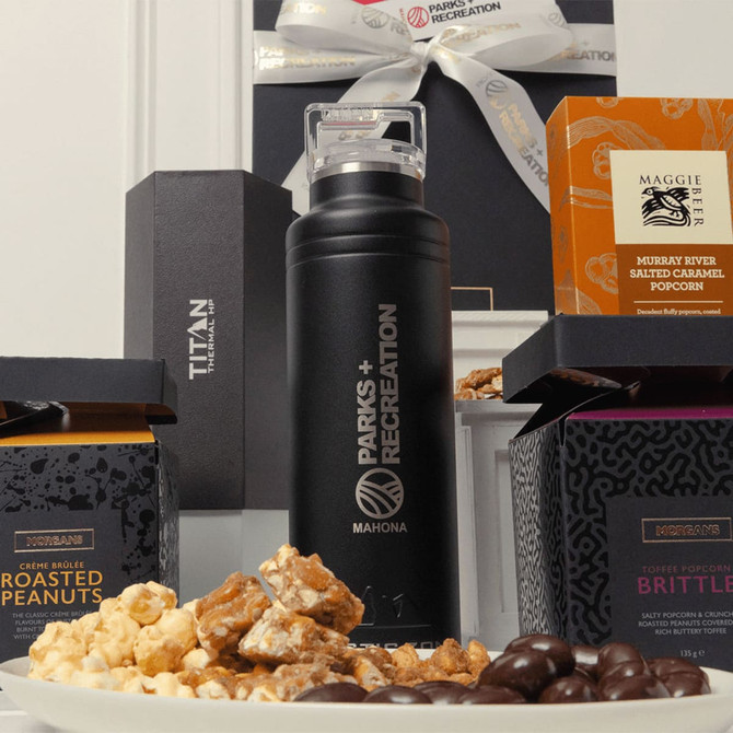 A black drink bottle surrounded by popcorn, roasted peanuts, and brittle in elegant packaging.