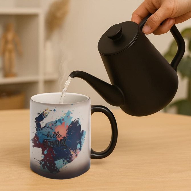 A black-handled mug featuring a vibrant colour-changing design, with hot liquid being poured from a kettle.