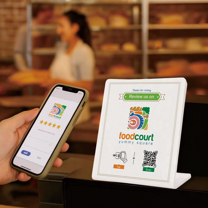 A white NFC review stand displayed on a counter, with a smartphone scanning a QR code nearby.