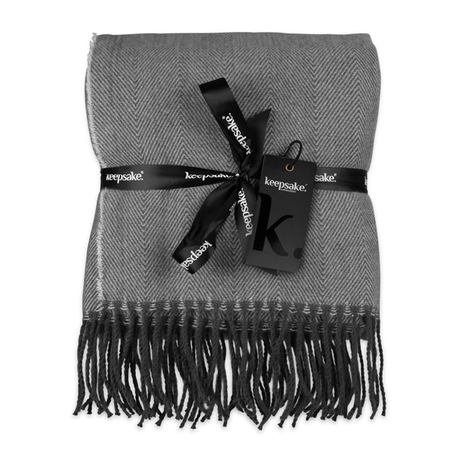 A grey herringbone throw blanket wrapped with a black ribbon and tag, featuring fringed edges.