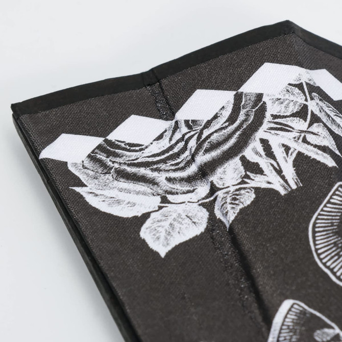 A bamboo fabric hand fan in black with white floral designs and a slim, folded structure. It features branding.