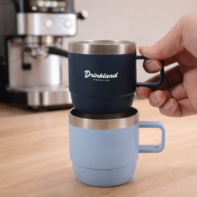 A stackable stainless steel mug set in navy and light blue, featuring a handle and a logo, displayed on a wooden surface.