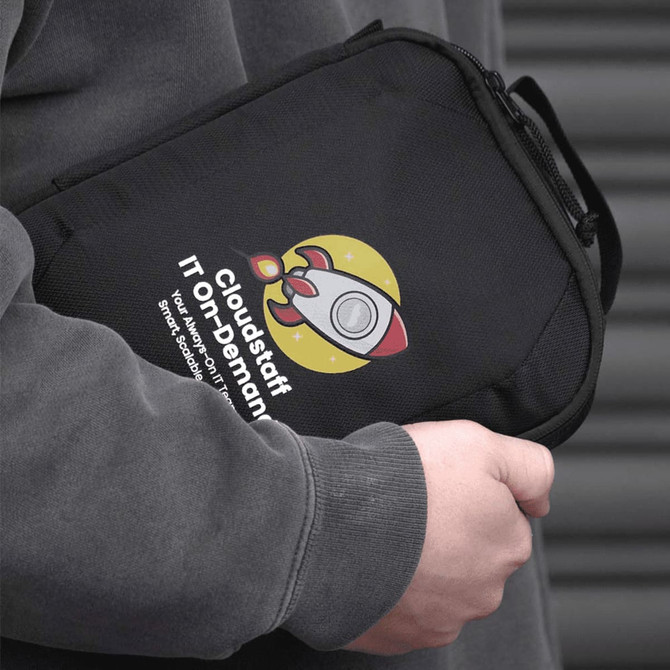 A black tech case with a logo, featuring a rocket design and a handle, held by a person in a grey hoodie.