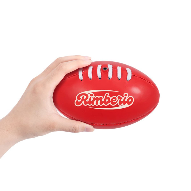A red mini Australian Rules ball being held in a hand, featuring a logo on its surface.
