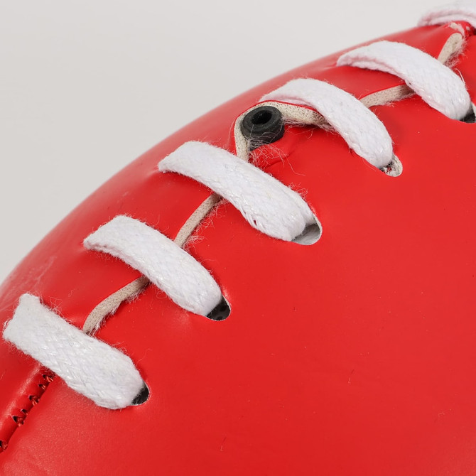 A red promotional Aussie Rules ball with white lacing and a smooth surface. It features a logo.
