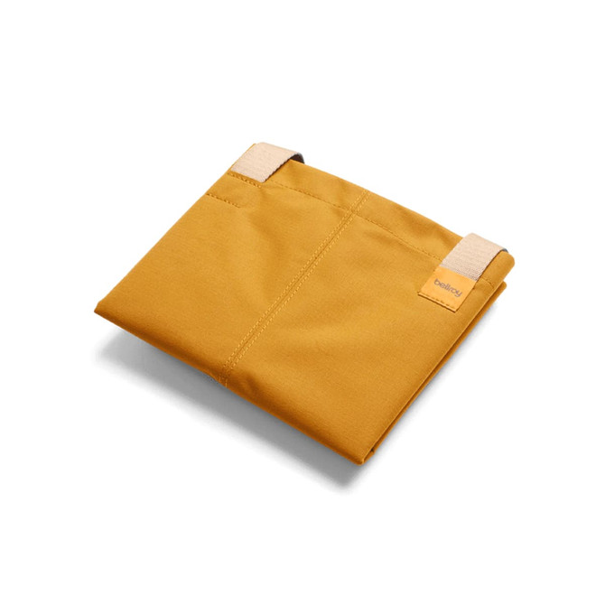 A mustard yellow tote bag with two straps, featuring a logo. The bag is folded and lying flat.