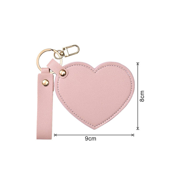 A pink heart-shaped compact mirror with a keychain attachment, featuring a smooth surface and gold accents.