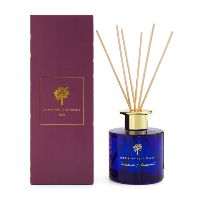 A reed diffuser with a blue glass bottle, gold lid, and bamboo reeds, packaged in a purple box.