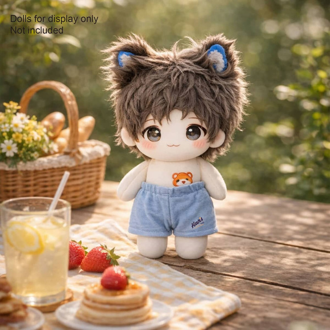 A plush doll wears blue shorts with a bear design, featuring fuzzy brown hair and ears, set outdoors with a picnic scene.