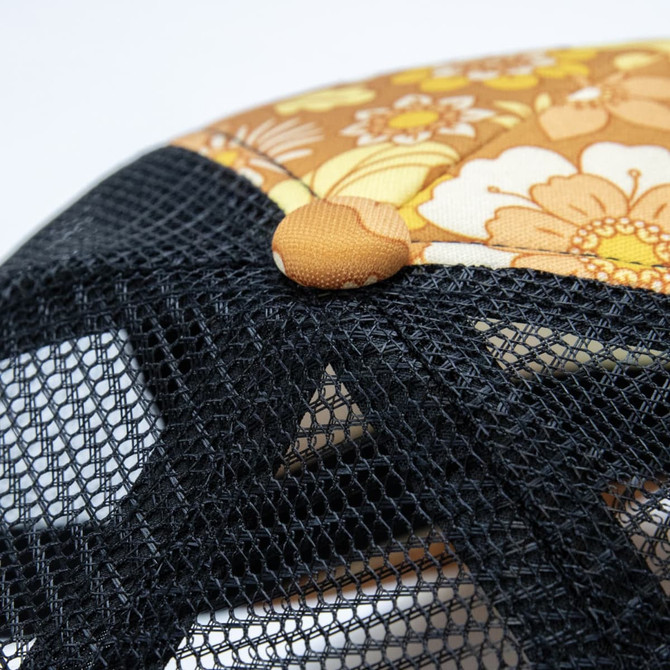 A trucker cap featuring a floral design in warm colours, with a black mesh back and a button on top.