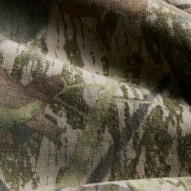 A close-up of fabric featuring a heavy faded camo pattern in green and brown tones.