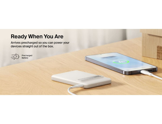A white power bank on a wooden surface, connected to a smartphone, with a visible logo.