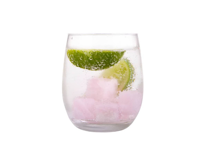 A glass filled with sparkling water, pink gin stones, and lime slices garnishing the drink.