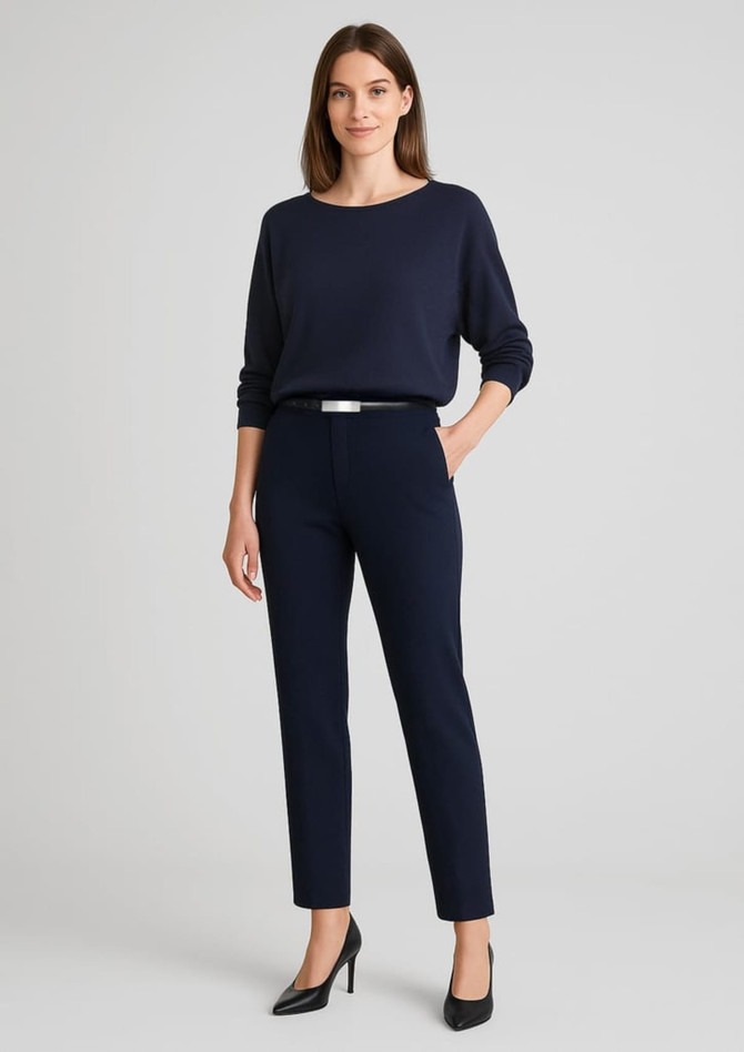 A woman wearing mid-rise pull-on pants in navy, paired with a black top and heels, with one hand on her hip.