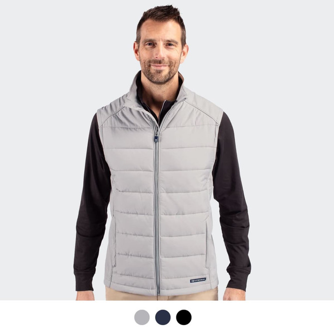 A man in a light grey quilted vest stands against a plain background. The vest features a branding logo.