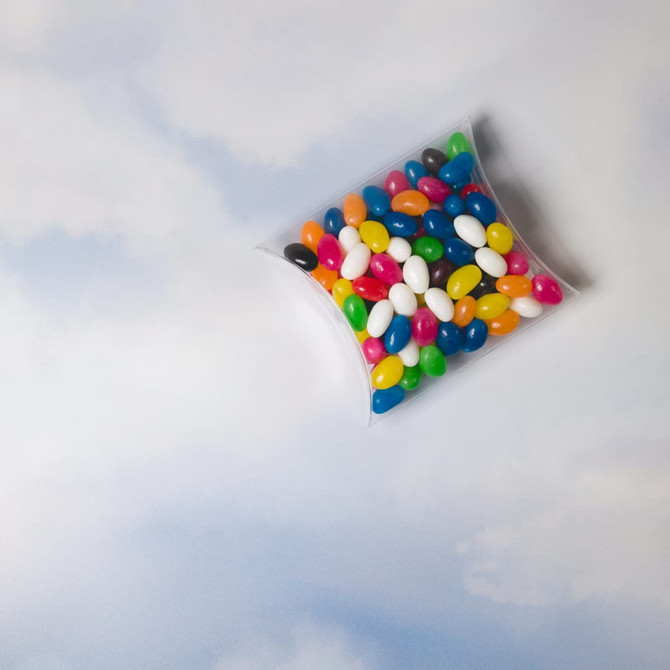 A pillow pack filled with assorted colour mini jelly beans, featuring vibrant hues of green, yellow, blue, pink, and black.