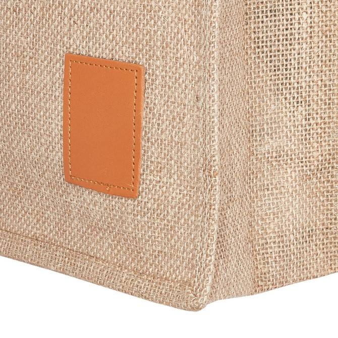 A jute bag in natural brown with a brown leather patch on the side, featuring a textured, woven design.