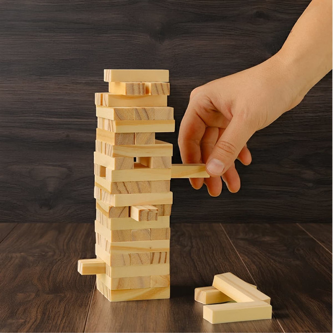 A large wooden tower set featuring light-coloured blocks stacked vertically, with a hand removing a block.
