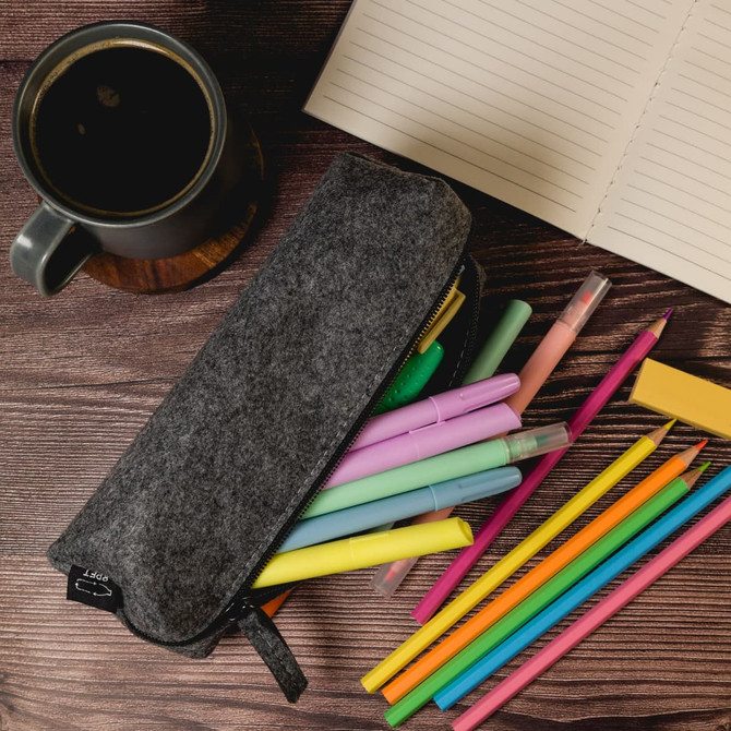 A grey felt utility case filled with colourful pens and markers, situated beside a coffee cup and an open notebook.