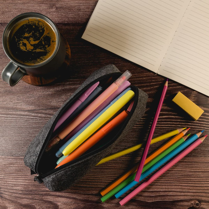 A grey felt utility case filled with colourful pens and pencils, alongside a notepad and a coffee cup.
