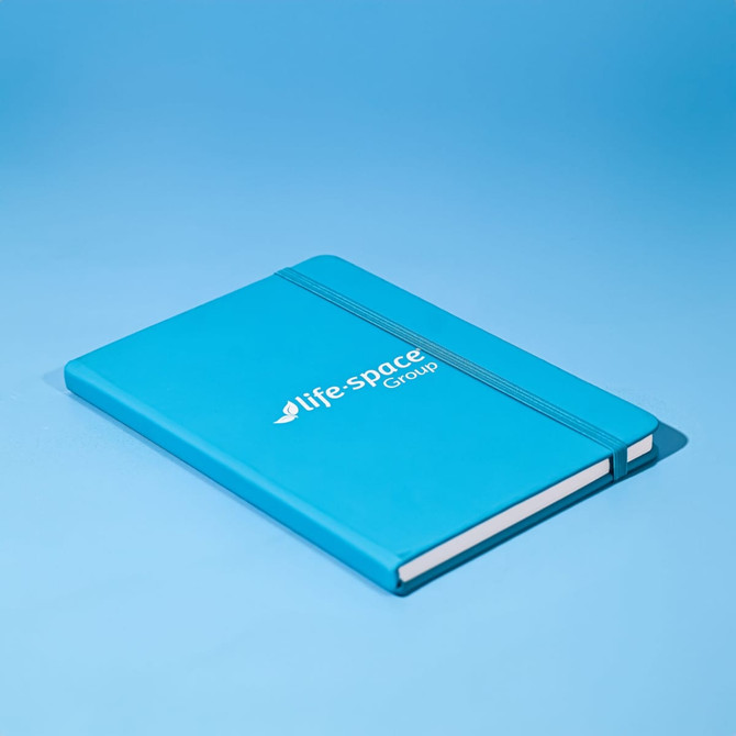 A blue A5 notebook with an elastic band closure and a branded logo on the cover.