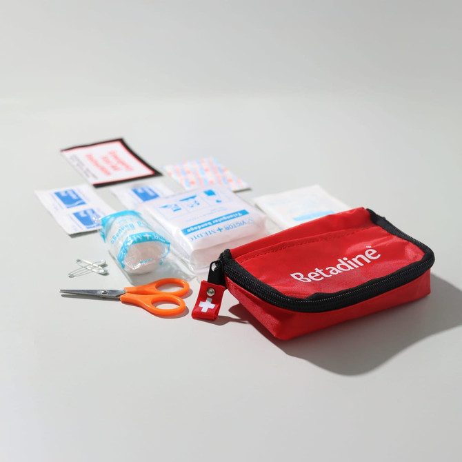 A red first aid kit with scissors, adhesive dressings, antiseptic wipes, and a roll of gauze. The kit includes a logo.