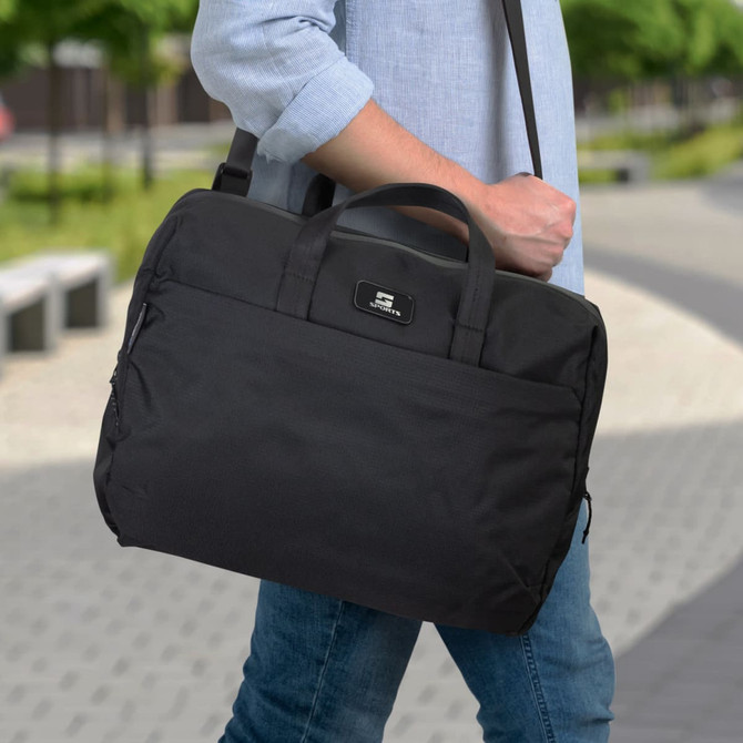 A black laptop bag with a shoulder strap and handles is being carried by a person outdoors. It features a branding logo.