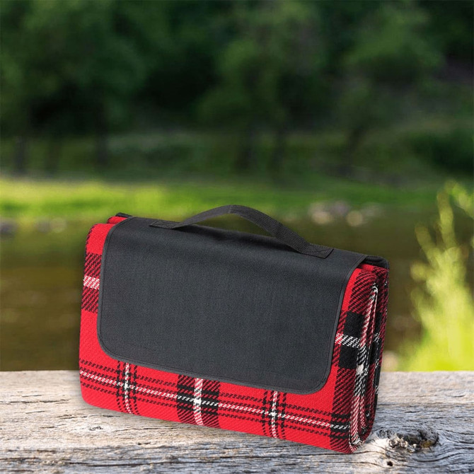 A red and black checked picnic rug with a black handle, resting on a wooden surface near water.