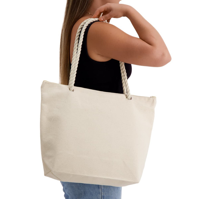 A cream-coloured tote bag with rope handles, held by a woman wearing a black top.
