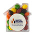 A clear acrylic house-shaped container filled with colourful Skittles in various shades. It features a logo on the front.