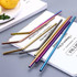 A set of stainless steel drinking straws in various metallic colours, arranged on a flat surface with some plates beside them.