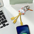 A custom-shaped PVC charging cable in yellow with a bunny keyring, resting on a desk next to a laptop and smartphone.
