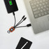 A square-shaped light-up charging cable with multiple connectors in orange, connected to a laptop and a smartphone.