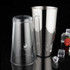 A cocktail shaker set featuring a transparent plastic cup and a shiny stainless steel shaker, placed on a dark surface with ice and fruit.
